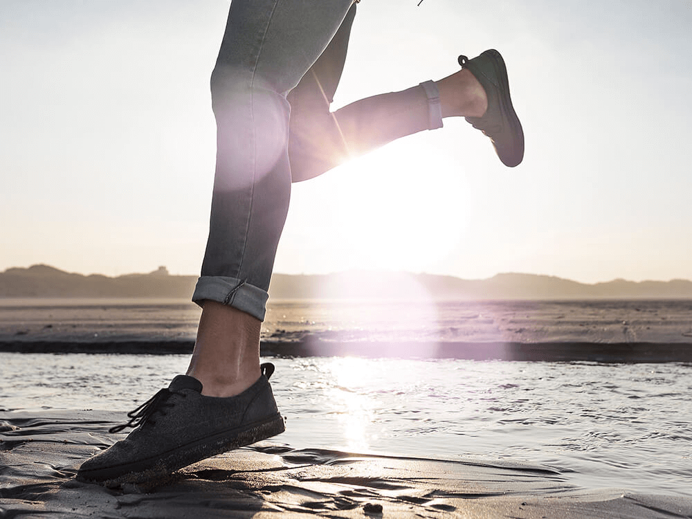 Frau läuft über den Strand mit Sneakers von der Marke Bleed.