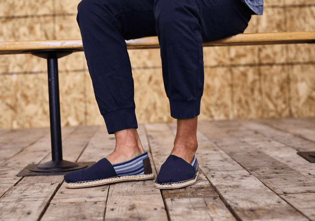 Mann sitzt auf Stuhl und trägt Schuhe von der Marke Toms - Espadrilles.